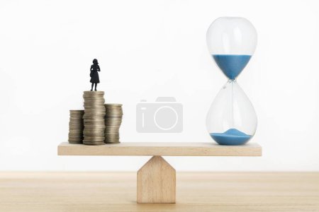 Téléchargez les photos : Concept de la valeur temporelle de l'argent. Horloge de sable et figurine de femme d'affaires sur des pièces empilées sur une scie à glace - en image libre de droit
