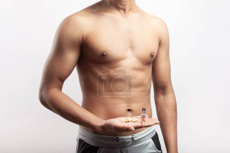 Foto de Un hombre delgado sin camisa sosteniendo una jeringa de esteroides anabólicos y pastillas para adelgazar en la palma de su mano - Imagen libre de derechos