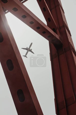 Téléchargez les photos : Un plan vertical du Golden Gate Bridge avec un avion volant au-dessus dans le ciel gris - en image libre de droit