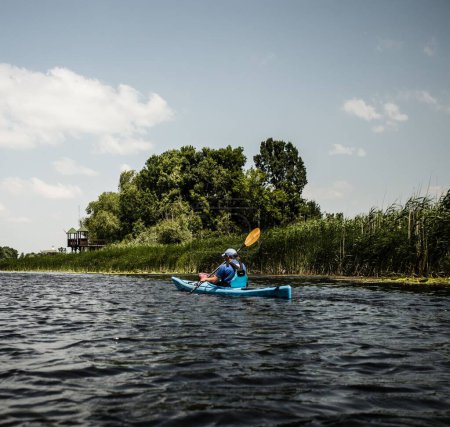 Photo for A man kayaking in the lake with surrounding greenery on a sunny day - Royalty Free Image