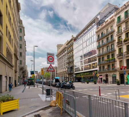 Téléchargez les photos : Une femme marchant sur le trottoir de l'ombre à Barcelone pendant la mi-journée un panoramique montrant les deux côtés de la rue avec de grands bâtiments - en image libre de droit