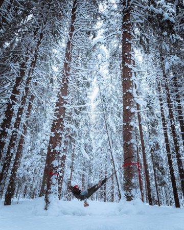 Téléchargez les photos : Un plan vertical d'une personne appréciant la neige tout en se balançant dans un hamac dans une forêt - en image libre de droit
