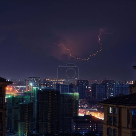 Téléchargez les photos : Un éclair éclatant dans le ciel au-dessus d'une ville moderne pendant la nuit - en image libre de droit