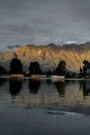 Téléchargez les photos : Le pittoresque lac Dal avec des péniches en bois et des montagnes reflétées dans l'eau claire par une journée nuageuse - en image libre de droit