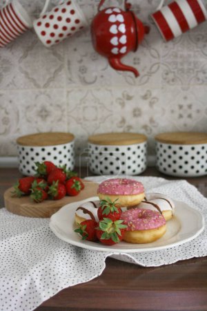 Photo for A vertical shot of strawberry-glazed donuts on a plate on the kitchen counter - Royalty Free Image