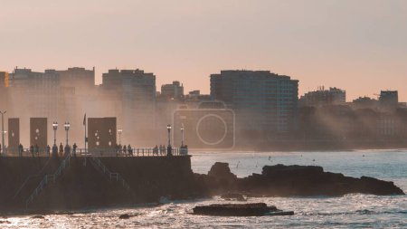 Foto de Paisaje marino con la ciudad de Gijón al fondo con gente caminando por la tarde - Imagen libre de derechos