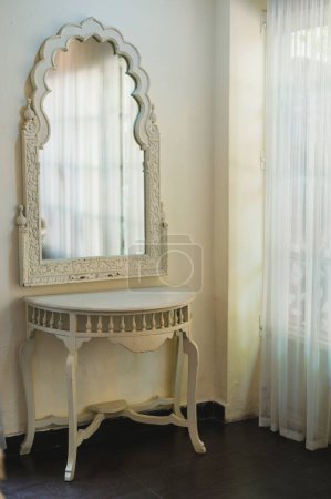 Téléchargez les photos : Un miroir vintage de forme élaborée avec des sculptures détaillées sur son cadre blanc dans une pièce antique - en image libre de droit