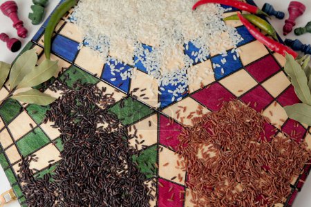 Photo for Still life of white rice, red rice and wild rice with bay leaves, chili peppers on a triple chessboard, with chess pieces in the background. - Royalty Free Image