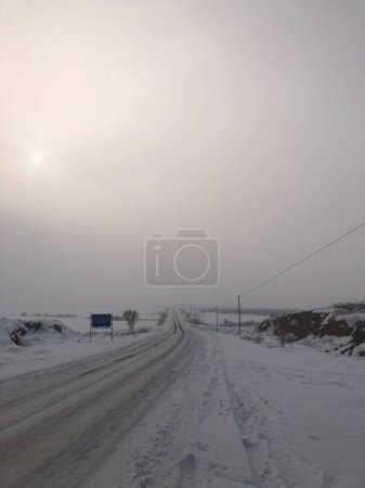 Photo for A beautiful vertical shot of highway in the center of valley covered with snow under foggy sky - Royalty Free Image