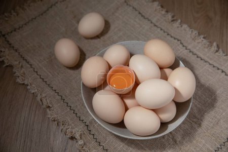 Téléchargez les photos : Une vue de dessus d'un œuf craqué sur une pile d'œufs frais sur une nappe - en image libre de droit
