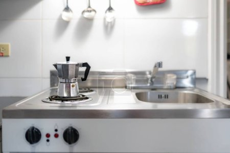 Foto de Una pequeña cocina con una cafetera italiana junto a un lavabo en los utensilios de cocina de fondo - Imagen libre de derechos