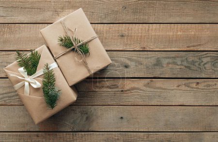 Téléchargez les photos : Photo plate de deux cadeaux de Noël enveloppés dans du papier brun et décorés avec une brindille d'épinette verte. Espace de copie sur fond en bois. - en image libre de droit