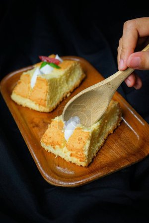 Téléchargez les photos : Doigt humain mangeant des morceaux moelleux de gâteau sur plateau en bois avec cuillère sur fond satin noir - en image libre de droit
