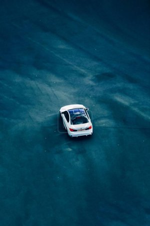 Téléchargez les photos : Plan vertical à angle élevé d'une BMW blanche conduisant sur une route bleuâtre foncé à l'extérieur - en image libre de droit