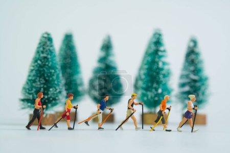 Téléchargez les photos : Les figures miniatures de randonneurs marchant tenant bâtons avec des arbres de Noël en arrière-plan - en image libre de droit