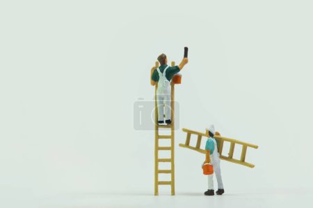 Miniaturfiguren von Bauarbeitern, die die Wände auf weißem Hintergrund bemalen