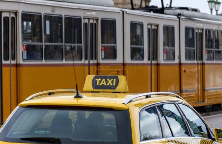Téléchargez les photos : Un tramway jaune passant par un taxi jaune garé dans la rue en ville - en image libre de droit