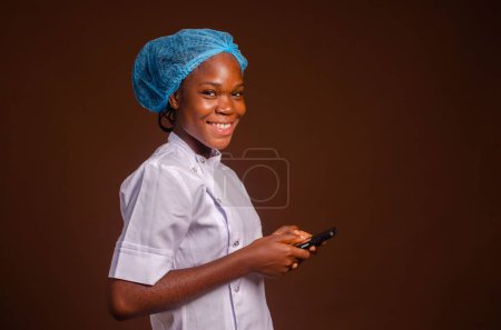 Photo for A beautiful portrait of a happy young doctor texting with a smartphone on a brown background - Royalty Free Image