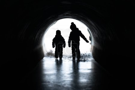 Téléchargez les photos : Enfants marchant dans le tunnel de l'obscurité à la lumière - en image libre de droit