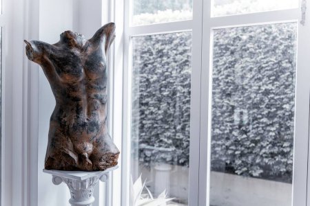 Téléchargez les photos : La vue d'une sculpture corporelle figurative nue en bronze placée près de la fenêtre - en image libre de droit