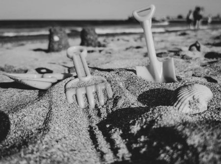 Téléchargez les photos : Un plan en niveaux de gris de pelle jouet de sable et râteau à la plage - en image libre de droit