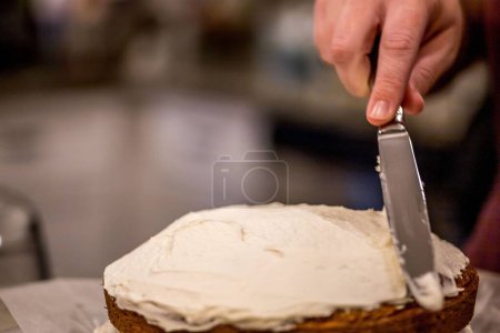 Photo for A shallow focus of a woman using metal butter knife to spread a cream on a cake - Royalty Free Image