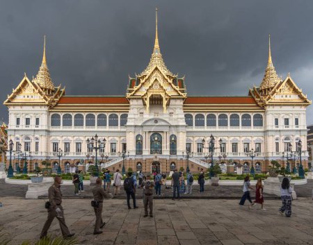 Photo for A group of people standing at the Chakri Maha Prasat Throne Hall of the Grand Palace Complex under gray cloudy sky - Royalty Free Image