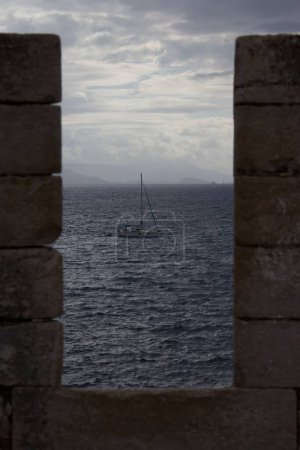 Foto de Un disparo vertical de un velero enmarcado entre las paredes de la antigua fortaleza de Corfú en un día nublado - Imagen libre de derechos