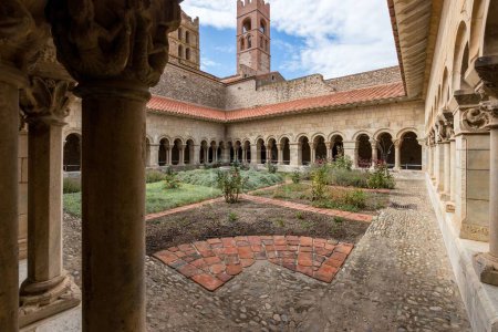 Téléchargez les photos : La cour de la cathédrale Elne à colonnade voûtée avec pavage pavé et plantes vertes - en image libre de droit