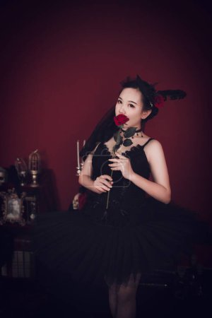 Téléchargez les photos : Un plan vertical d'une belle fille asiatique de l'Est portant une robe noire tutu et tenant une rose tout en regardant la caméra - en image libre de droit