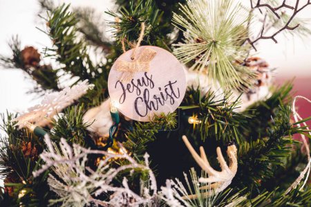Foto de Un primer plano de un juguete de madera con el nombre de "Jesucristo" en un árbol de Navidad decorado - Imagen libre de derechos