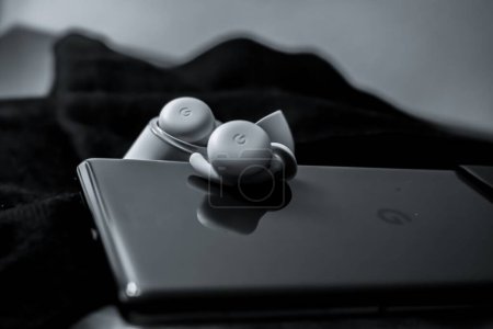 Téléchargez les photos : Un cliché en niveaux de gris Google Pixel Buds avec un appareil mobile sur des couvertures noires et blanches - en image libre de droit