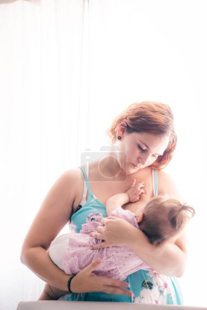 Photo for A young mother breastfeeding her baby in a sunny room - Royalty Free Image