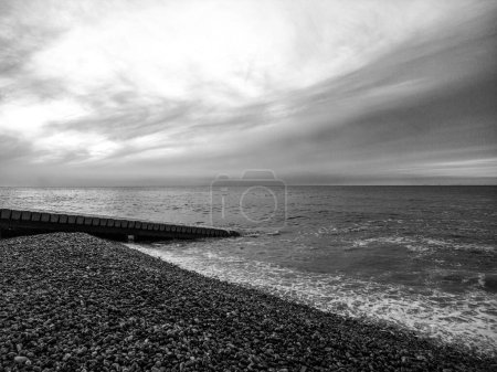 Téléchargez les photos : Échelle de gris d'une plage rocheuse avec des vagues de mer peu profondes frappant le rivage avec de la mousse - en image libre de droit