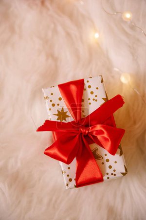 Foto de Una vista superior de una caja de regalo de Navidad con un lazo rojo en el paño suave decorado con luces - Imagen libre de derechos