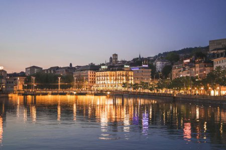 Téléchargez les photos : Le soir Zurich illuminé bâtiments reflétés sur l'eau calme sous le ciel bleu - en image libre de droit