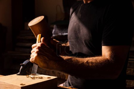 Téléchargez les photos : Gros plan des mains de l'homme à l'aide d'un ciseau et d'un maillet sur un morceau de bois - concept d'artisanat - en image libre de droit