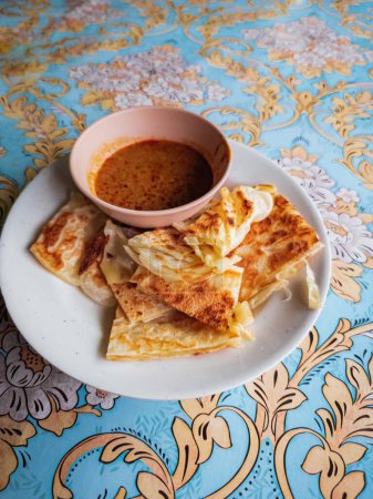 Photo for A vertical shot of a hot roti canai served with bowl of curry on a patterned tablecloth - Royalty Free Image