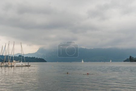 Téléchargez les photos : Les gens nagent près d'un quai avec des bateaux dans le paisible lac des Quatre-Cantons - en image libre de droit