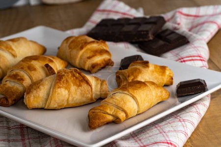 Foto de Un hermoso primer plano de croissants recién horneados en un plato con barras de chocolate negro - Imagen libre de derechos