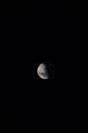 Foto de Un disparo vertical de la luna en una fase gibbous menguante que aparece en el oscuro, cielo negro - Imagen libre de derechos