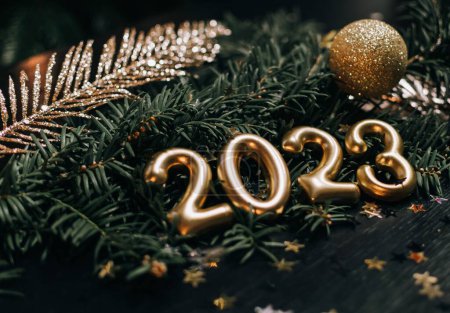 Foto de Fotografía de bodegón de primer plano de números dorados y decoraciones para el año nuevo 2023. Bola de oro y decoraciones en rama de pino verde oscuro. - Imagen libre de derechos