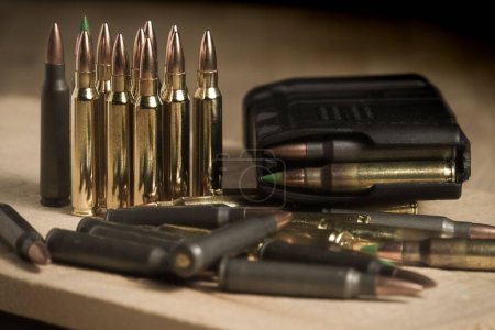Various 223 caliber (5.56mm) bullets standing or laying next to a full AR-15 magazine full of ammo