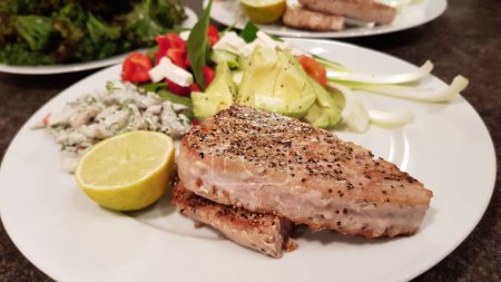 Photo for A closeup of freshly cooked tuna with salad and avocado on a plate on the table - Royalty Free Image