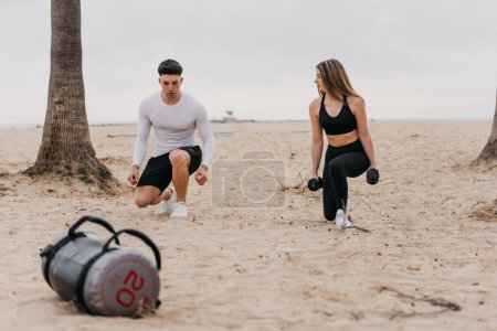 Photo for A young athletic couple exercising at the beach, doing lunges with dumbells - Royalty Free Image