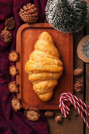 Photo for A top view of a croissant on a wooden plate with Christmas decorations - Royalty Free Image