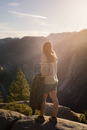 Photo for A vertical shot of a female standing on a rock and admiring the waterfall view at sunset - Royalty Free Image