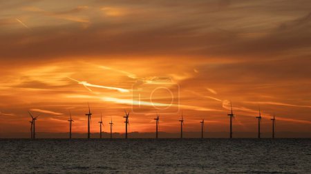 Foto de Rico cielo naranja sobre un parque eólico en alta mar en el Mar del Norte. Las turbinas eólicas se siluetean contra el cielo colorido. - Imagen libre de derechos