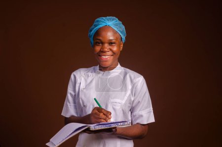 Foto de Un primer plano de una hermosa enfermera sonriendo y tomando notas sobre un fondo marrón - Imagen libre de derechos