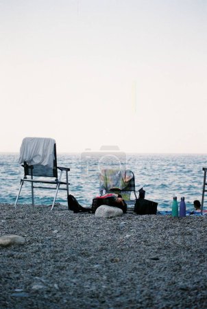 Foto de Las dos sillas con varias ropas y bolsas en la playa rocosa - Imagen libre de derechos